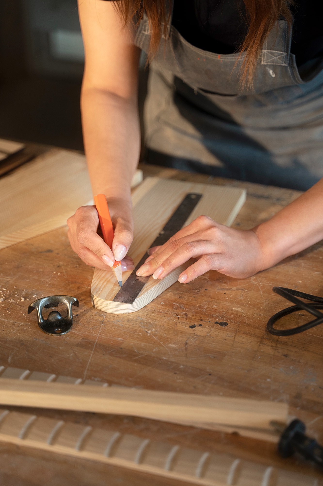 Frau zeichnet mit Bleistift und Lineal auf einem Holzstück in einer Tischlerei